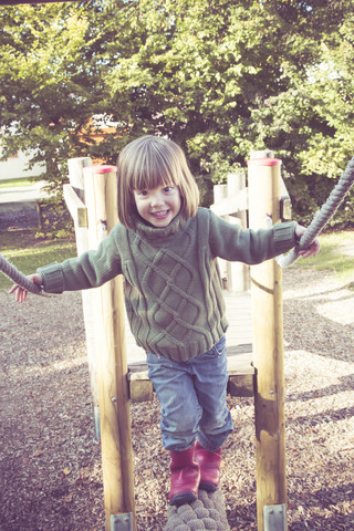 Kleines Mädchen klettert auf Spielplatzgerät, lizenzfreies Stockfoto