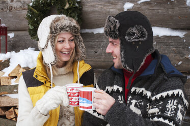 Couple clinking cups at wooden hut in winter - HHF004948