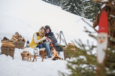 Lächelndes Paar im Schnee am Lagerfeuer - HHF004951