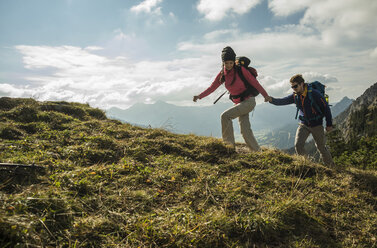 Austria, Tyrol, Tannheimer Tal, young couple hiking hand in hand on alpine meadow - UUF002257