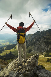 Austria, Tyrol, Tannheimer Tal, young woman with hiking poles cheering on mountain top - UUF002280