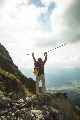 Österreich, Tirol, Tannheimer Tal, junge Frau mit Wanderstöcken jubelnd auf Berggipfel, lizenzfreies Stockfoto