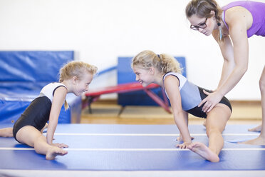 Trainer mit zwei Mädchen bei einer Gymnastikübung am Boden - ZEF001315