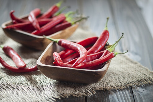 Wooden bowl of red chili peppers on jute and wood - SBDF001331