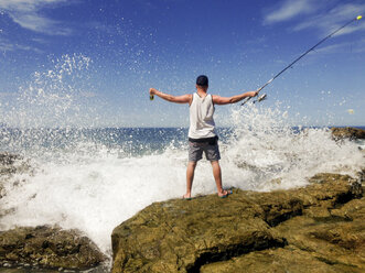 Junger Mann mit Angelrute an der mexikanischen Pazifikküste, Wellen brechen am felsigen Ufer. - ABAF001511
