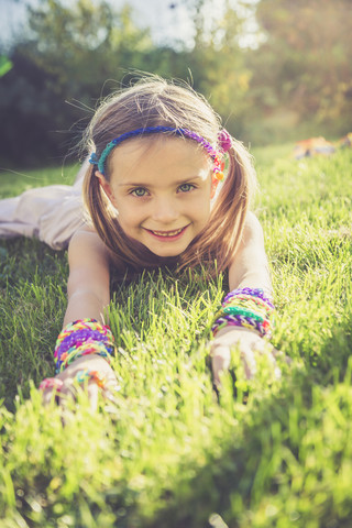 Portrait of smiling little girl with loom bracelets and hair-band lying on a meadow stock photo