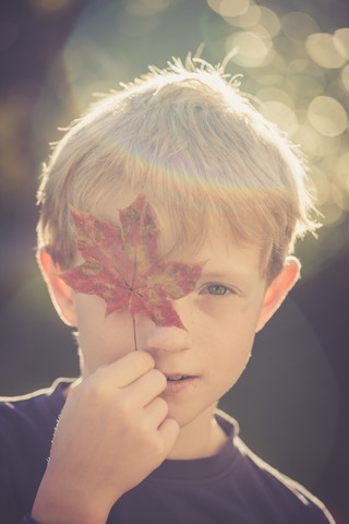 Porträt eines Jungen, der ein Auge mit einem Herbstblatt bedeckt, lizenzfreies Stockfoto
