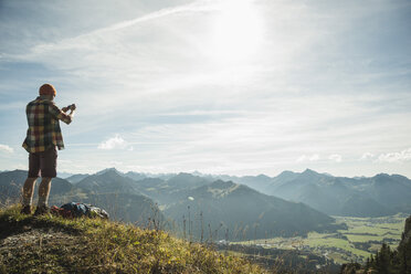 Austria, Tyrol, Tannheimer Tal, young man taking picture in mountainscape - UUF002194