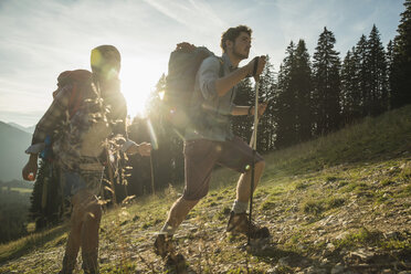 Austria, Tyrol, Tannheimer Tal, young couple hiking in sunlight on alpine meadow - UUF002212