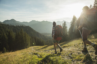 Austria, Tyrol, Tannheimer Tal, young couple hiking in sunlight on alpine meadow - UUF002145