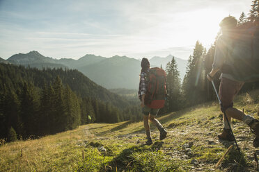 Österreich, Tirol, Tannheimer Tal, junges Paar wandert im Sonnenlicht auf Almwiese - UUF002145