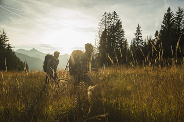 Österreich, Tirol, Tannheimer Tal, junges Paar wandert im Sonnenlicht auf Almwiese - UUF002208