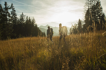 Austria, Tyrol, Tannheimer Tal, young couple hiking in sunlight on alpine meadow - UUF002143