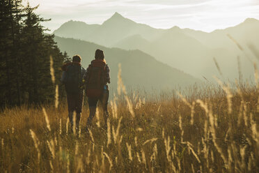 Österreich, Tirol, Tannheimer Tal, junges Paar wandert im Sonnenlicht auf Almwiese - UUF002142