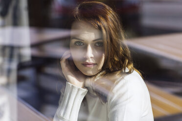 Portrait of young woman looking through window pane of a cafe - GDF000511
