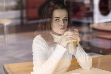 Porträt einer jungen Frau mit Latte Macchiato, die in einem Café sitzt und durch eine Fensterscheibe schaut - GDF000509