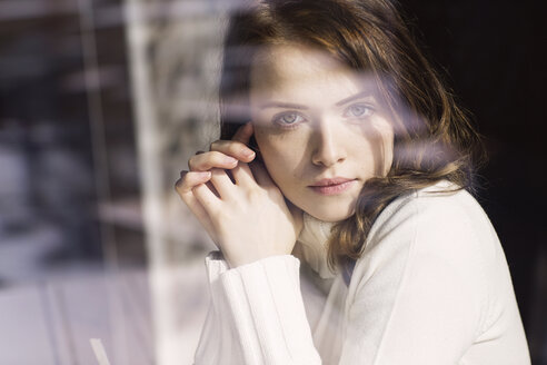 Portrait of young woman looking through window pane of a cafe - GDF000508