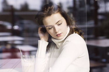 Porträt einer jungen Frau mit Latte Macchiato, die in einem Café sitzt und durch eine Fensterscheibe schaut - GDF000507