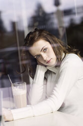 Porträt einer jungen Frau mit Latte Macchiato, die in einem Café sitzt und durch eine Fensterscheibe schaut - GDF000504