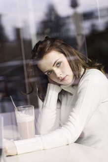 Portrait of young woman with Latte Macchiato sitting in a cafe looking through window pane - GDF000504