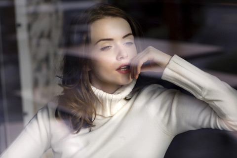 Porträt einer nachdenklichen jungen Frau, die durch die Fensterscheibe eines Cafés schaut, lizenzfreies Stockfoto