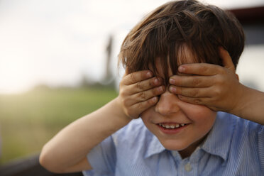 Porträt eines lächelnden kleinen Jungen, der seine Augen mit den Händen bedeckt - FKIF000061