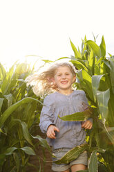 Grinsendes kleines Mädchen läuft durch ein Maisfeld - FKIF000065