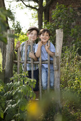 Portrait of two little boys standing behind a wooden fence - FKIF000040