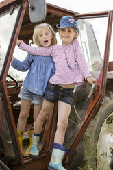 Porträt von zwei lächelnden kleinen Mädchen, die auf einem Traktor stehen - FKIF000076