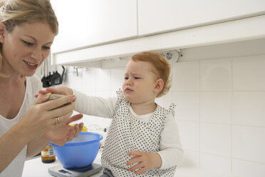 Mutter und kleine Tochter mit Smartphone in ihrer Küche - FSF000237