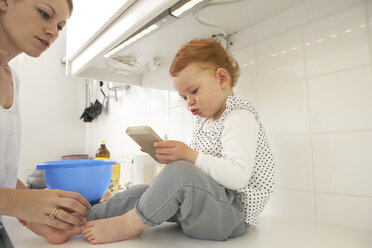 Little girl sitting on kitchen counter with smartphone - FSF000239