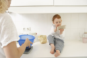 Little girl sitting on kitchen counter with smartphone - FSF000249