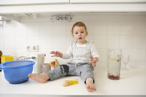 Kleines Mädchen sitzt auf Küchentisch mit zerbrochenem Ei, lizenzfreies Stockfoto