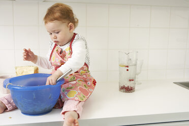 Kleines Mädchen sitzt mit Rührschüssel auf dem Küchentisch - FSF000218