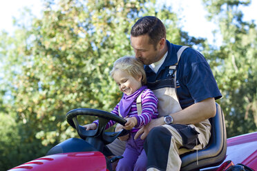 Vater und kleine Tochter fahren gemeinsam auf dem Rasenmäher - JFEF000502