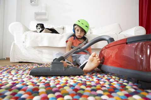 Erschöpfter Junge im Wohnzimmer mit Katze und Staubsauger, lizenzfreies Stockfoto