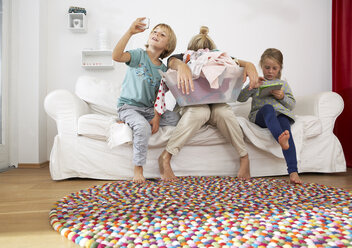 Erschöpfte Mutter mit Wäschekorb auf der Couch mit Kindern, die ein digitales Tablet und ein Mobiltelefon benutzen - FSF000270