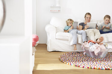 Mother, daughter and son on couch using digital tablet and cell phone with laundry basket on floor - FSF000263
