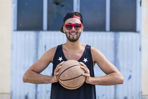 Porträt eines lächelnden jungen Mannes mit Basketball, der Basecap und Sonnenbrille trägt - DAWF000169