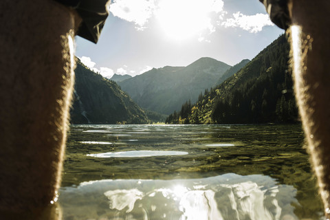 Österreich, Tirol, Tannheimer Tal, Beine eines Mannes am Seeufer, lizenzfreies Stockfoto
