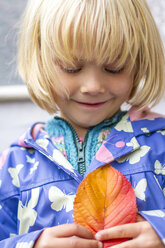 Porträt eines lächelnden kleinen Mädchens, das mit einem Herbstblatt späht - JFEF000494