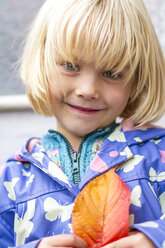 Porträt eines lächelnden kleinen Mädchens, das mit einem Herbstblatt späht - JFEF000495