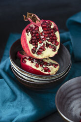Stack of bowls and two halves of a pomegranate on blue cloth - MYF000642