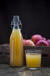 Flasche und Glas Apfelsaft und Kasten mit roten Äpfeln vor dunklem Hintergrund - LVF002073