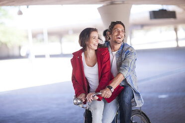Happy couple riding bicycle in parking garage - ZEF007945