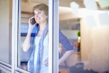 Female creative professional telephoning while looking through window - ZEF001499