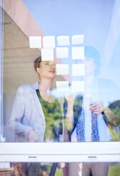 Zwei weibliche Kreativschaffende mit Haftnotizen hinter einer Fensterscheibe - ZEF001508