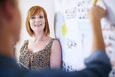 Female creative professional listening explanation of her colleague in front of whiteboard - ZEF002011