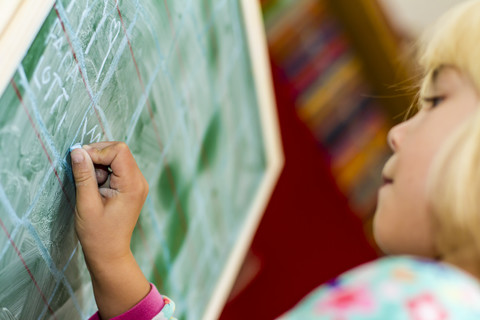 Kleines Mädchen schreibt an die Tafel, lizenzfreies Stockfoto