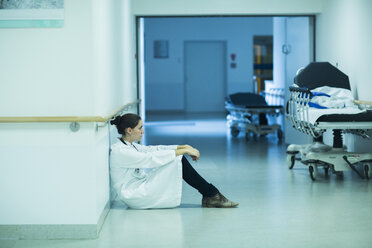 Überforderter junger Arzt sitzt auf dem Krankenhausflur - SGF000911